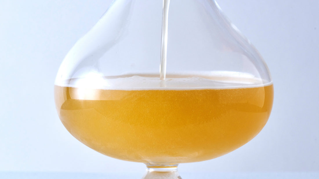 Golden craft beer being poured into a wide-bowl thistle glass, demonstrating the bulbous shape that enhances carbonation and foam retention.