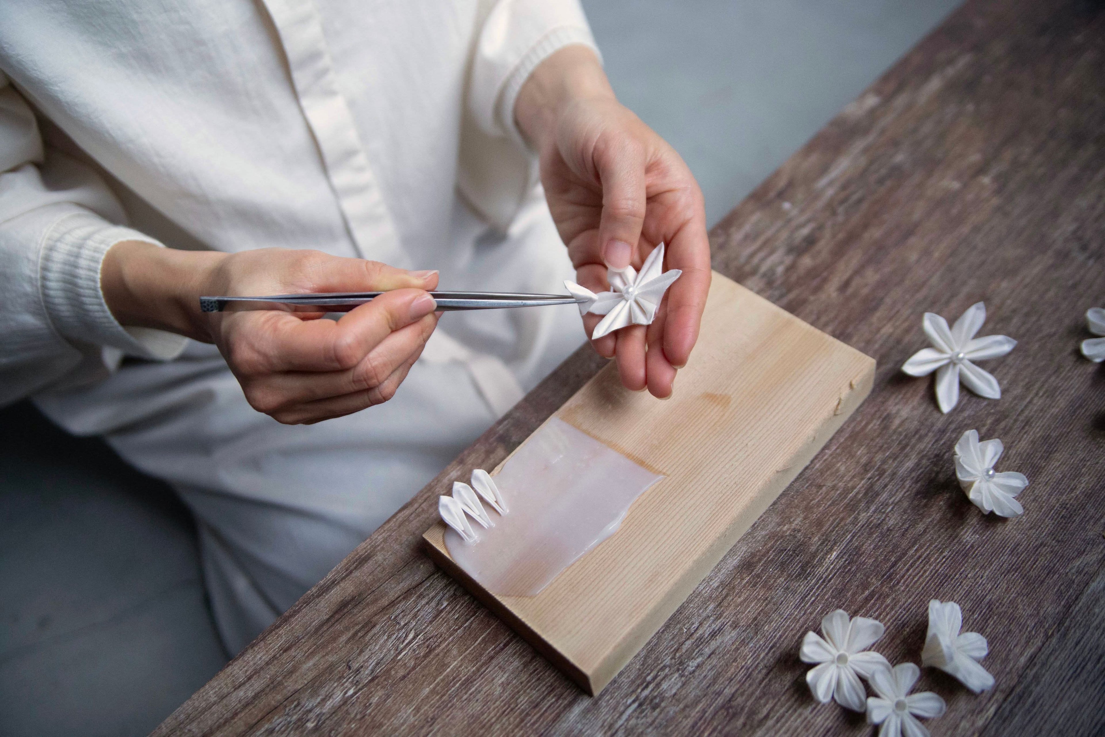 Artisan crafting Kaminoka Type A washi paper flowers with tweezers on a wooden board