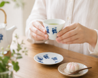 Person holding Shichifuku sencha teacup with saucer and wagashi sweet on wooden table, lifestyle