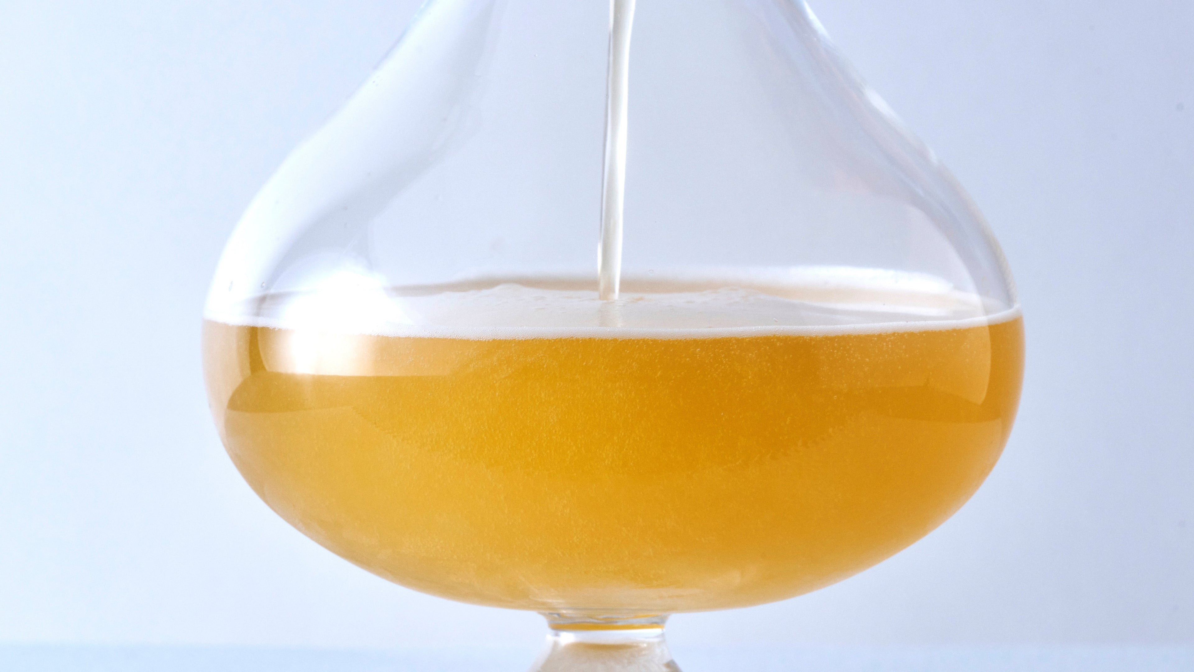 Golden craft beer being poured into a wide-bowl thistle glass, demonstrating the bulbous shape that enhances carbonation and foam retention.