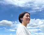 Woman with a blue earring against a blue sky with white clouds