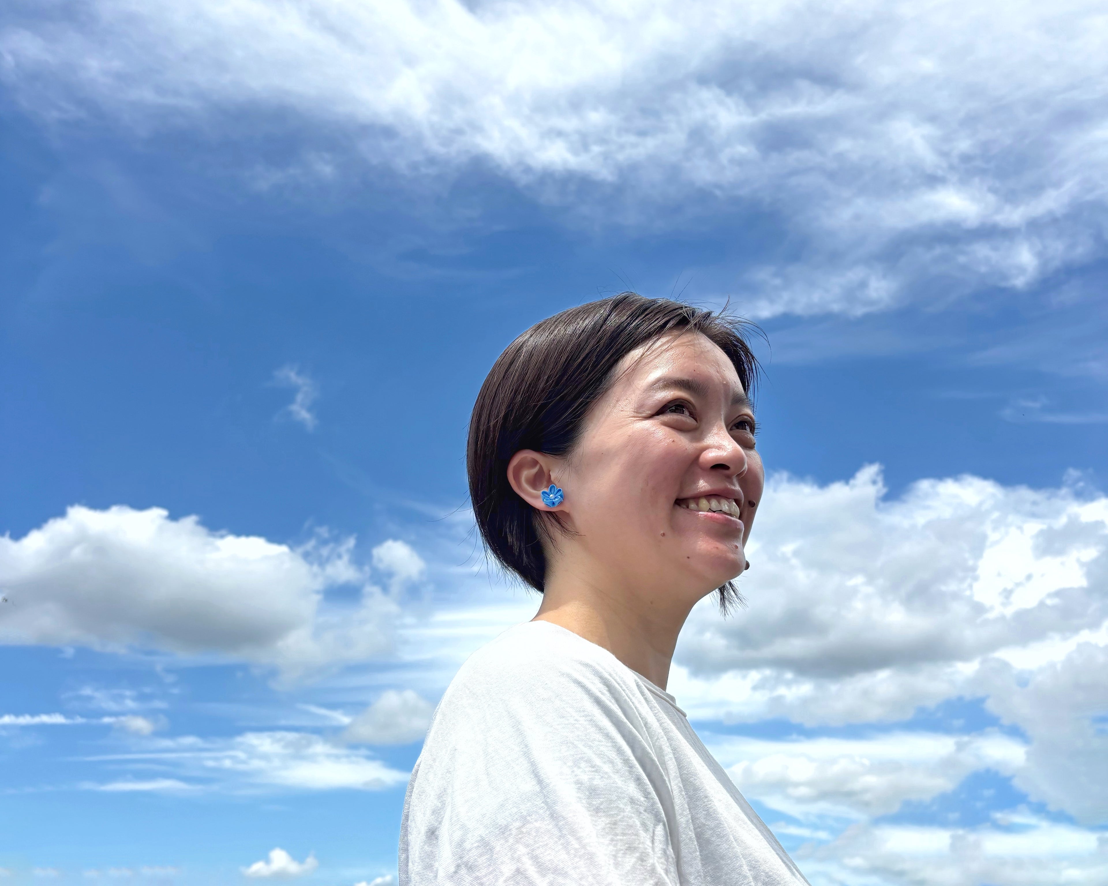 Woman with a blue earring against a blue sky with white clouds
