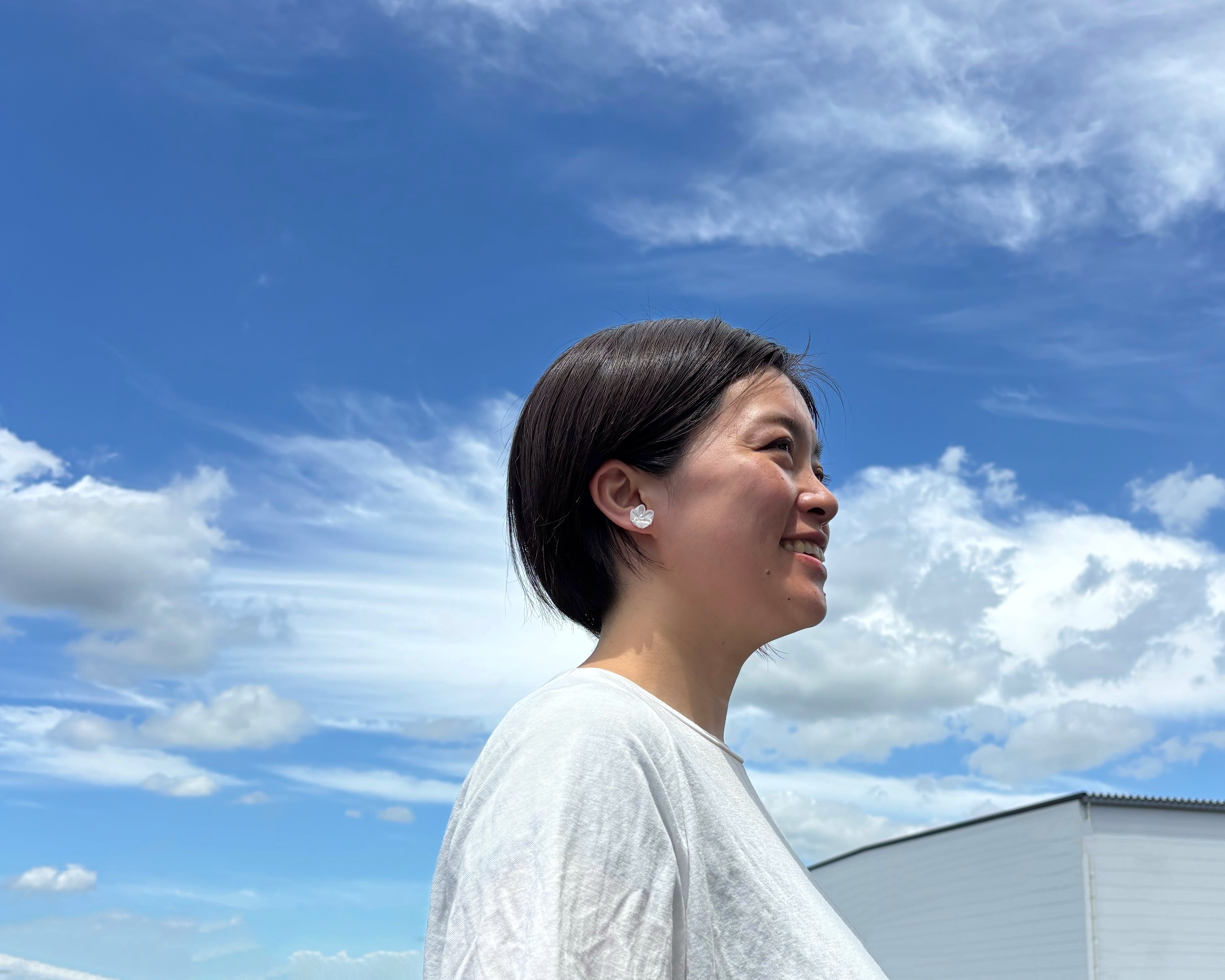Woman with short hair standing against a blue sky with clouds