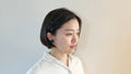 Woman with short black hair wearing a white shirt against a light background