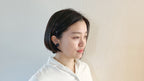 Woman with short black hair wearing a white shirt against a light background