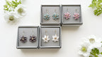 Floral earrings in gray boxes on a white background with flowers.