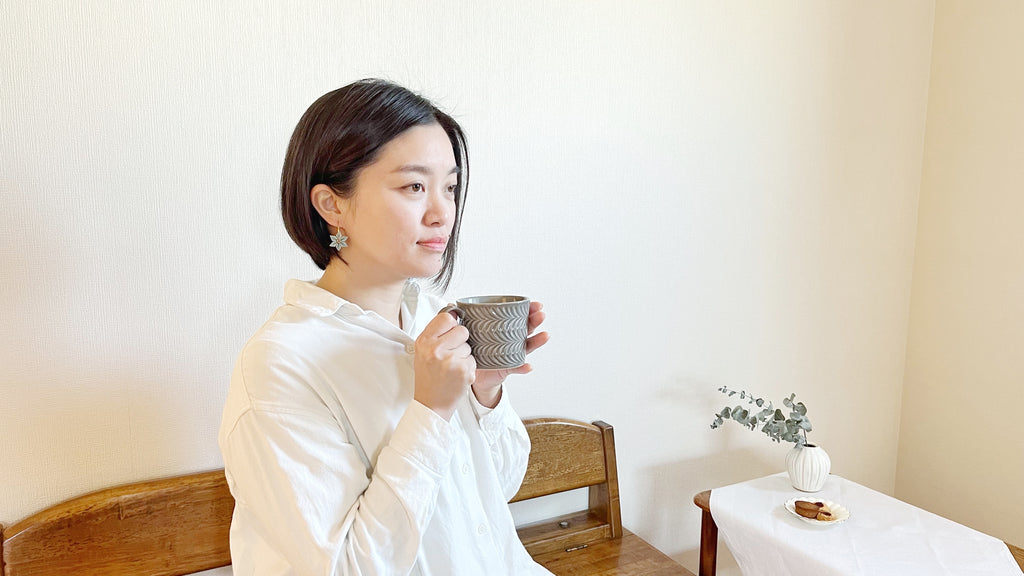 Woman holding a mug in a room with a wooden bench and plant.