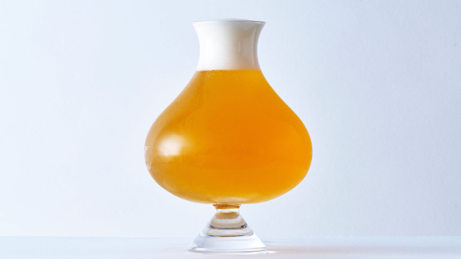 Handcrafted specialty beer glass filled with golden amber ale and a thick creamy white foam head, professional craft beer presentation.