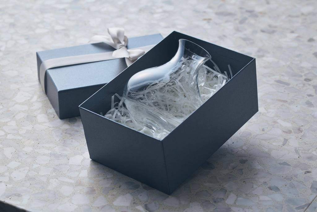 A premium handblown beer glass packaged in a minimalist blue gift box with white paper filler and a silk ribbon.