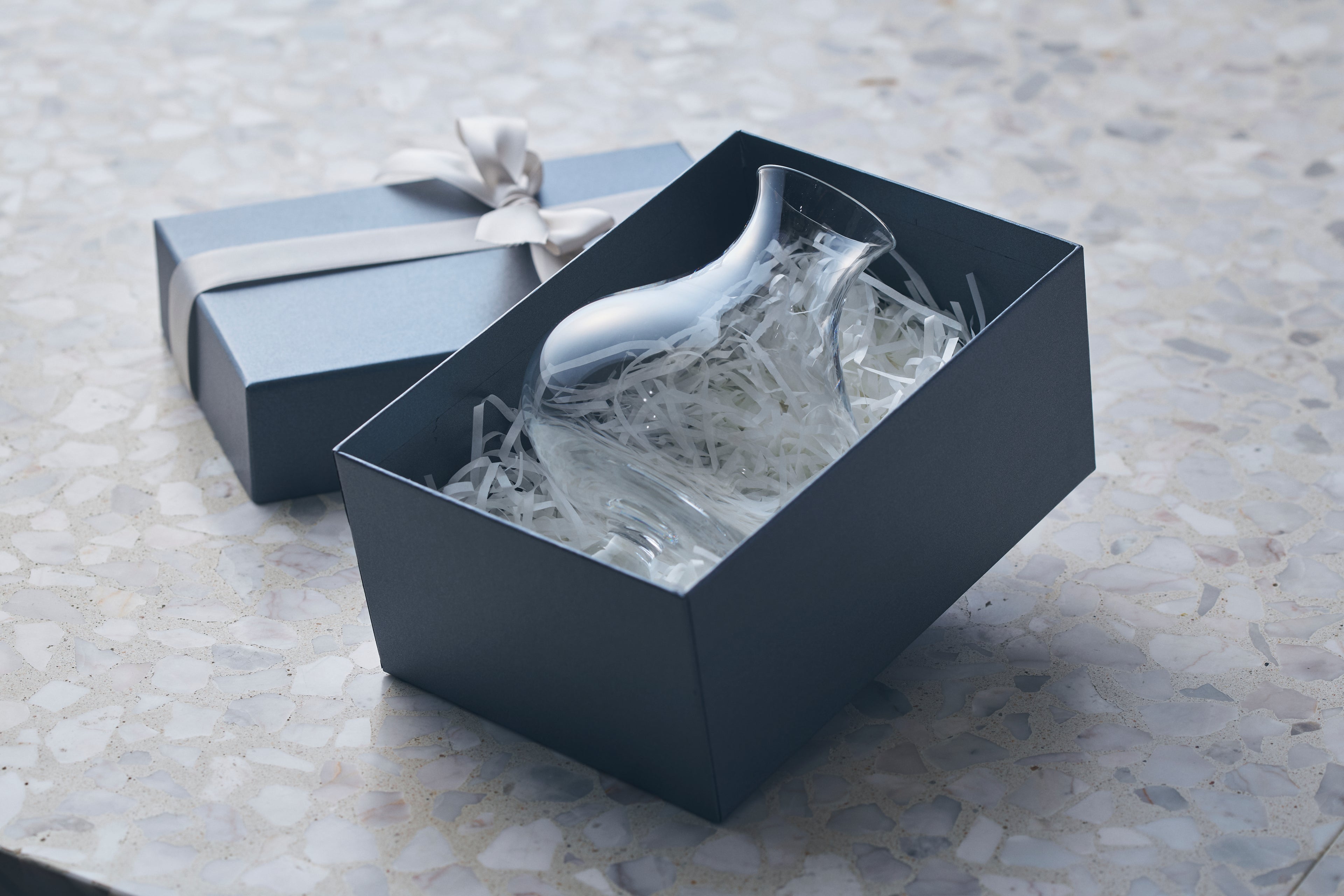 A premium handblown beer glass packaged in a minimalist blue gift box with white paper filler and a silk ribbon.