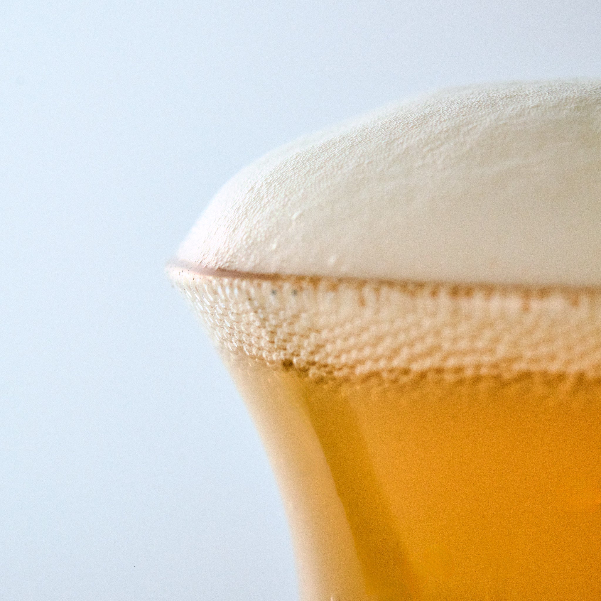 Handcrafted specialty beer glass filled with golden amber ale and a thick creamy white foam head, professional craft beer presentation.