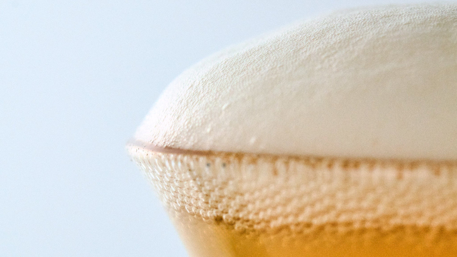 Macro view of thick, velvety beer foam rising above the rim of a specialty craft beer tulip glass.