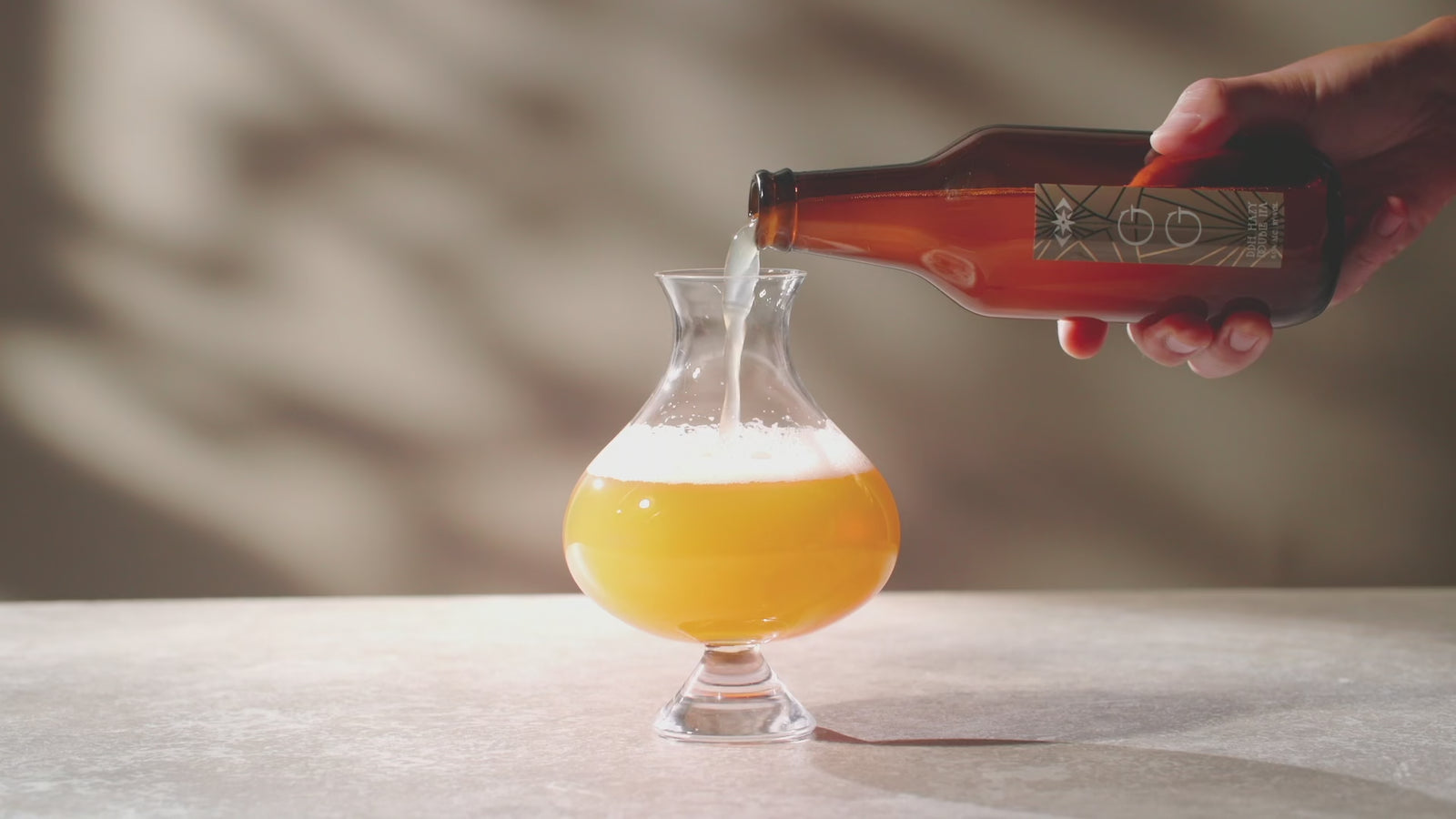 Perfect beer pour slowly of craft beer from a brown glass bottle into a unique handblown glass chalice, showing craft beer carbonation and foam head formation.