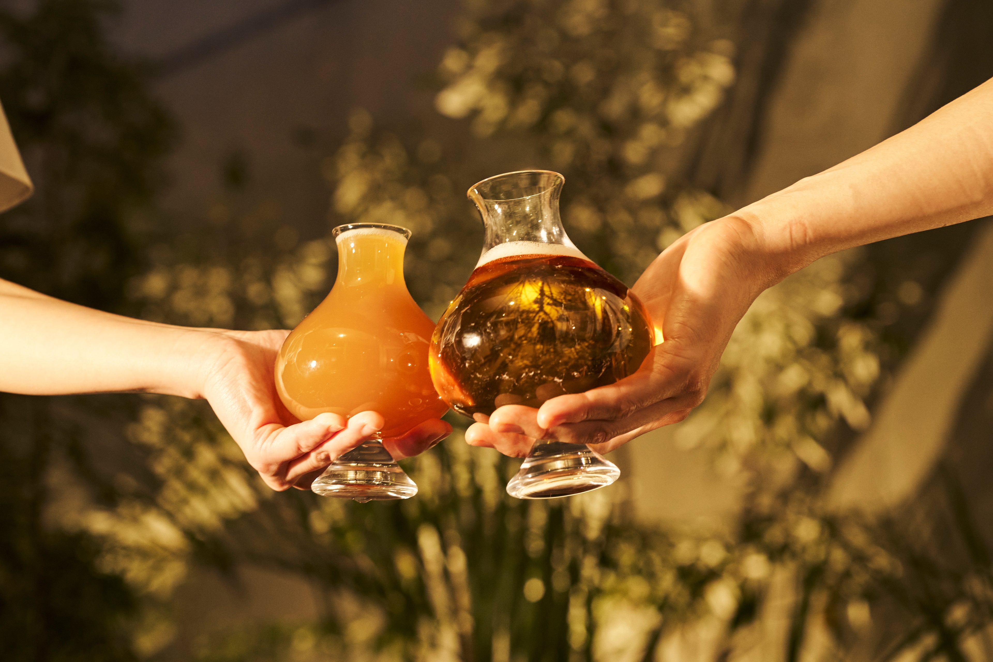 Two hands holding artisanal Japanese beer glasses in a 'cheers' gesture, emphasizing the emotional connection and the tactile beauty of Tokyo-based craftsmanship.