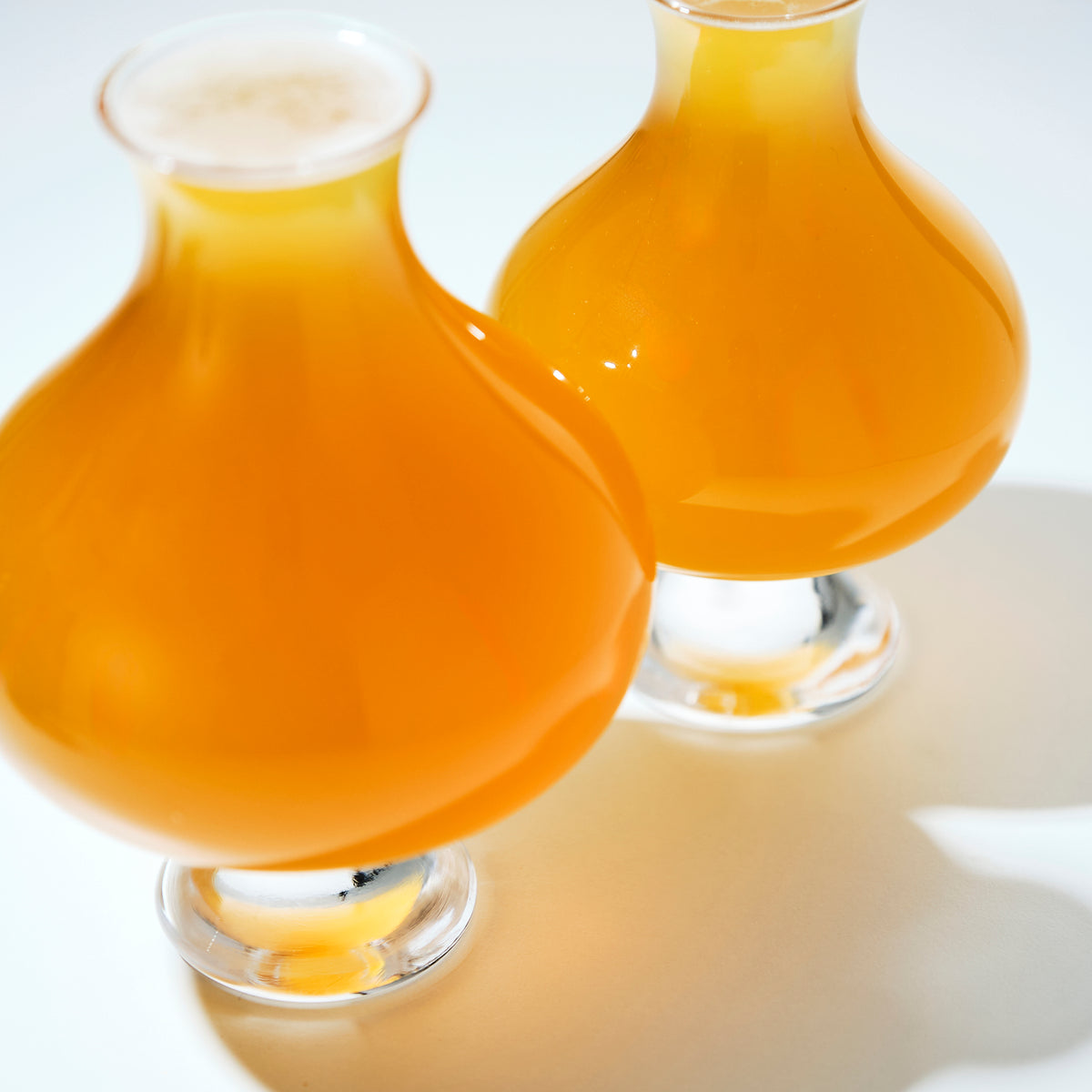 High-angle view of two filled tulip-style beer glasses, highlighting the vibrant orange hue of the craft ale.