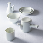 Minimalist **plain white Japanese porcelain dinnerware and tea set** including a teapot, cup, bowl, small pitcher, and stacked plates.