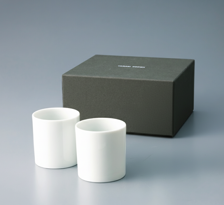 Pair of white Japanese Yunomi teacups presented next to the dark gray retail gift box or packaging.