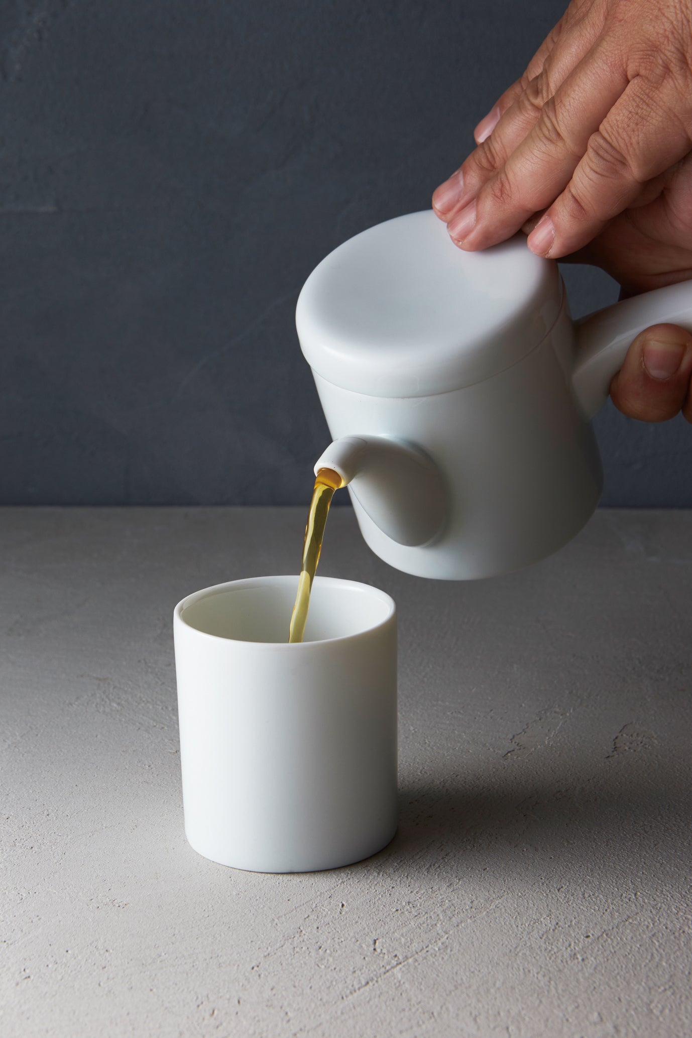 Close-up of the white Japanese porcelain teapot pouring tea into a matching Yunomi cup.