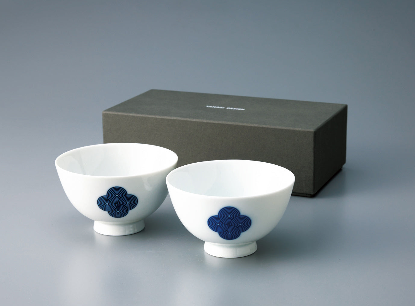 Pair of **Japanese porcelain rice bowls** with a footed base, decorated with the **blue and white Sometsuke swirl pattern**, displayed in front of the gift box.