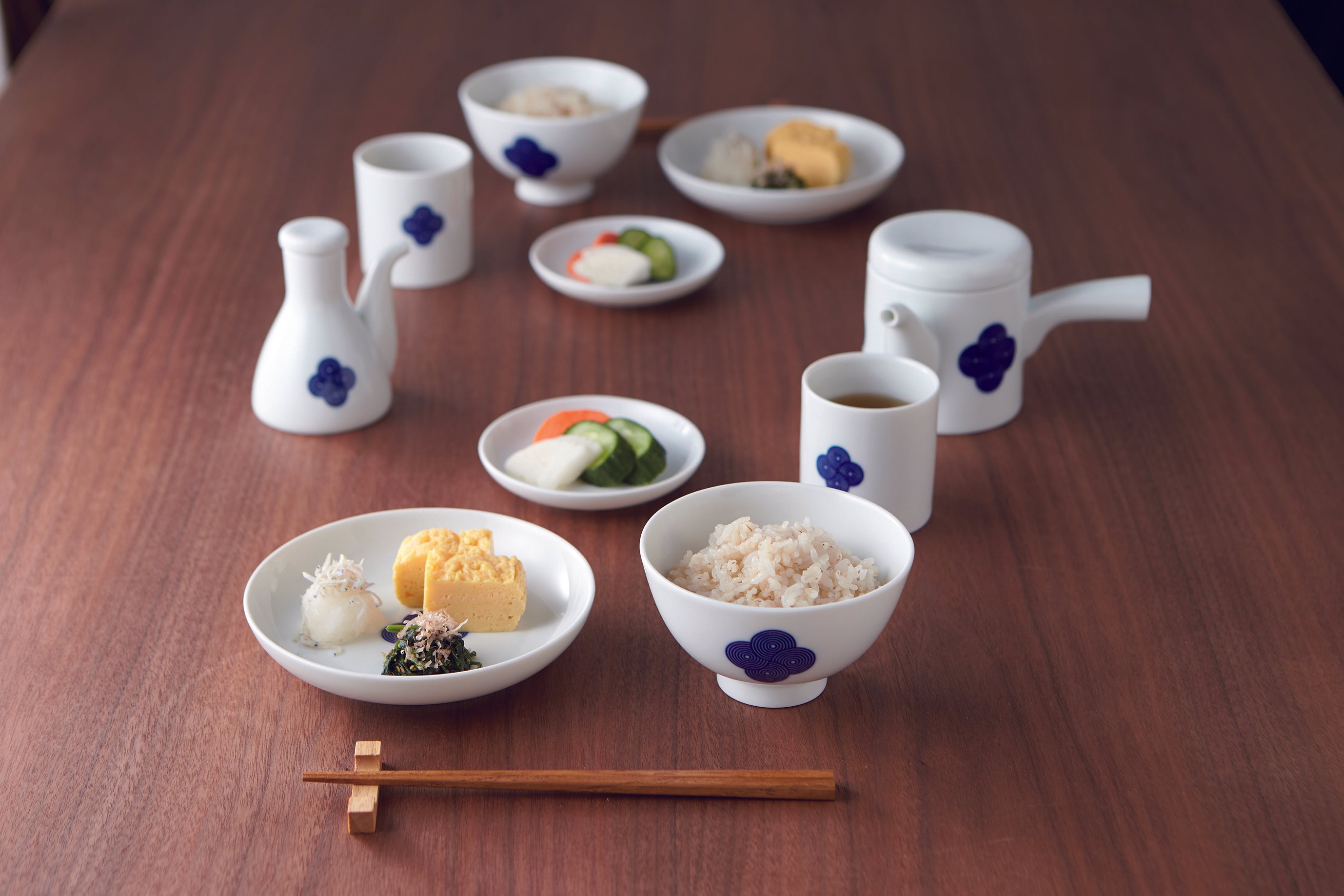 Full set of **Japanese Sometsuke porcelain tableware** arranged on a wooden table, featuring bowls of rice, plates of tamagoyaki and pickles, and a teapot, all with the blue and white swirl pattern.